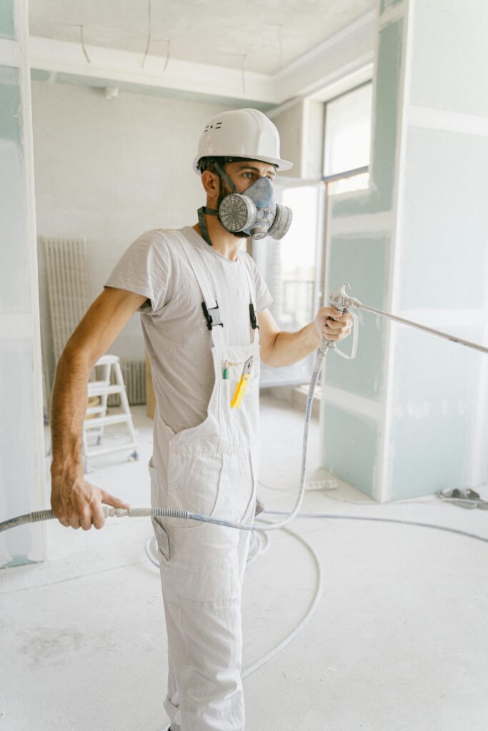 A construction worker wearing a gas mask and holding a hose in a renovation site.