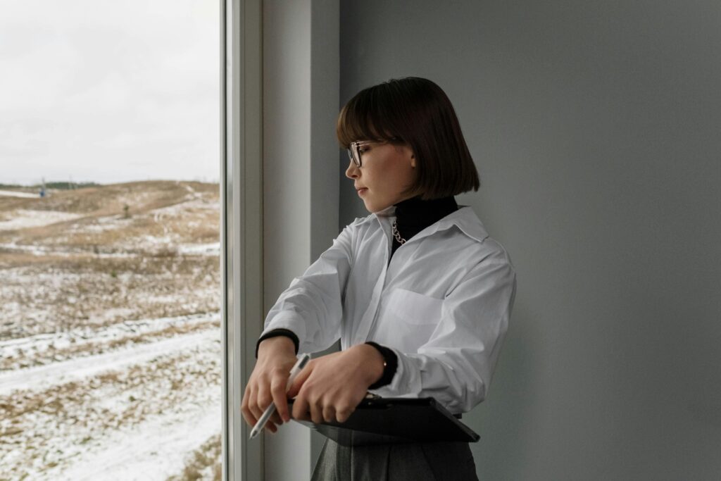 Architect looking outside a window on a snowy winter day, holding a clipboard.
